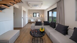 A modern living room with a sofa, a coffee table with fruit and drinks, a staircase, and a large window. - Armour Eclectic Villa (Platanias)
