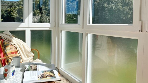 A room with large windows, a table with a magazine, a mug, and a chair.