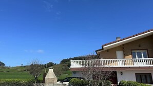 A two-story house with a balcony, a chimney, and a stone structure in the foreground.