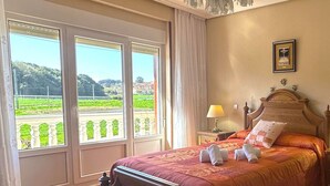 A bedroom with a large window, a bed with a wooden headboard, and a nightstand with a lamp.