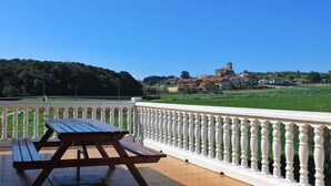 A terrace with a wooden picnic table and a white balustrade overlooking a village with a church.