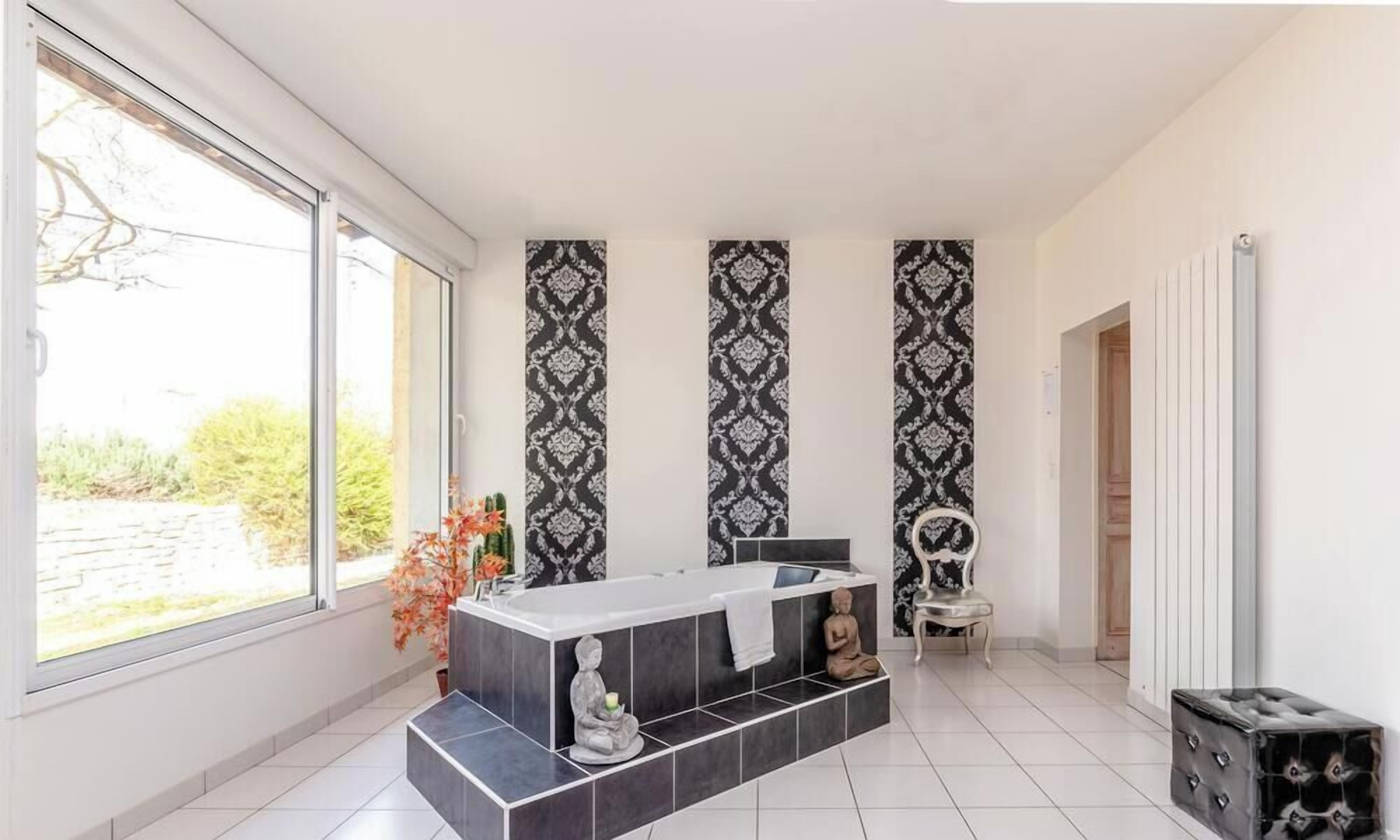 Un baño moderno con un ventanal grande, una bañera independiente y estatuas decorativas.
