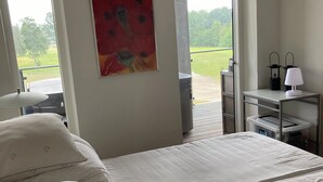 Un dormitorio con una cama, un cuadro, una ventana y una mesita de noche con una lámpara.