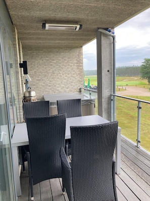 A balcony with a table and chairs, a heater, a water dispenser, and a view of a golf course.