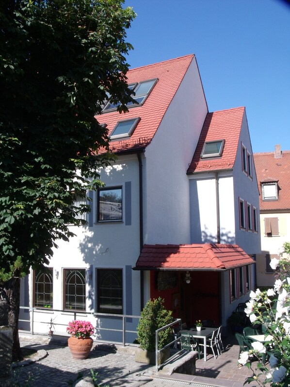 A two-story building with a red-tiled roof, a balcony, and a small outdoor seating area with chairs and tables. - Hotel Brehm (Würzburg)
