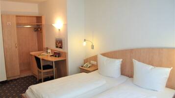 A hotel room with a bed, a desk, a chair, a wardrobe, and a nightstand with a phone.