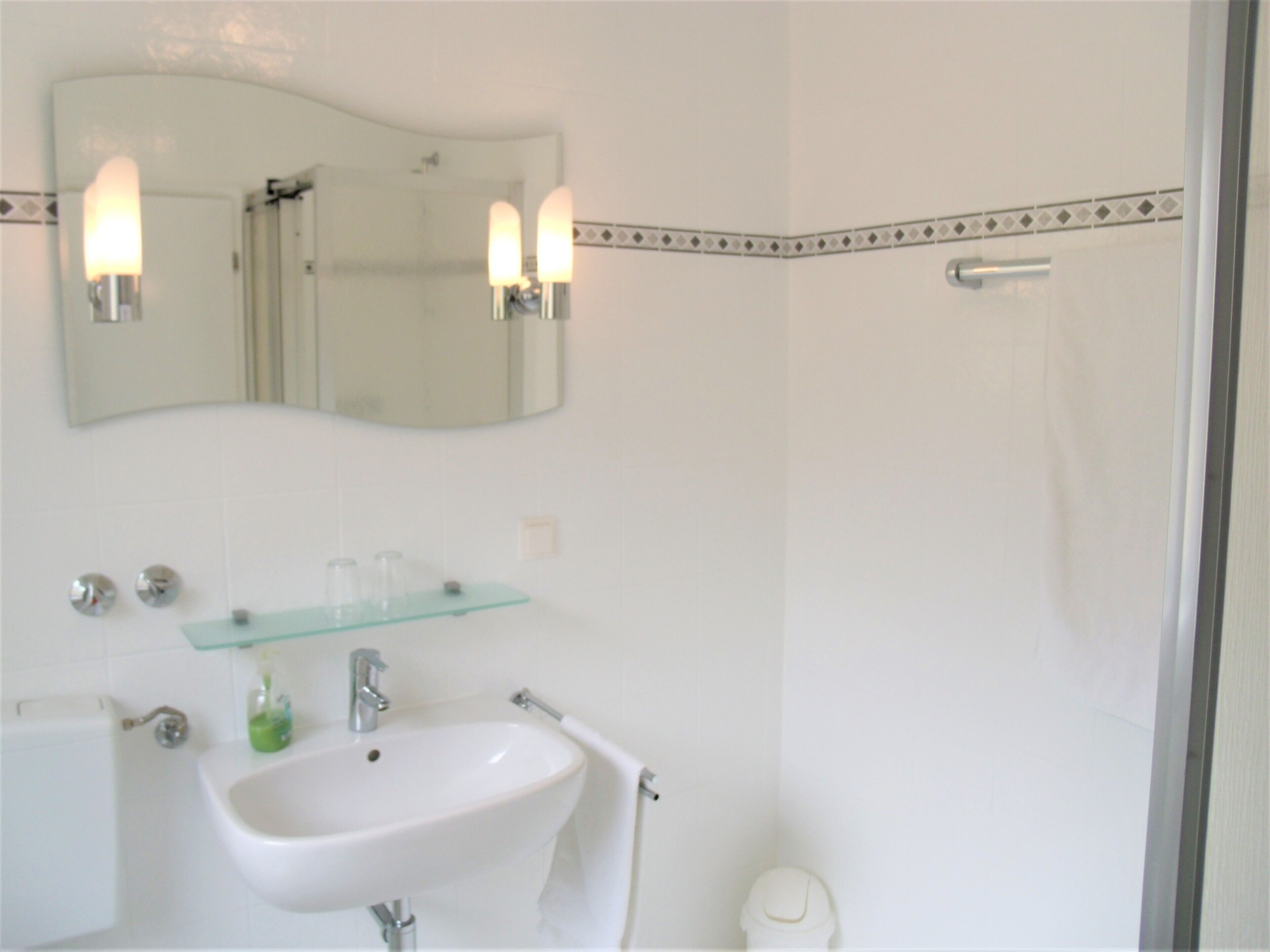 Une salle de bain avec un lavabo blanc, une étagère en verre, un miroir et un espace douche.
