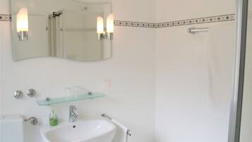 Une salle de bain avec un lavabo blanc, une étagère en verre, un miroir et un espace douche.