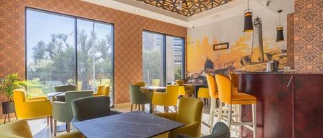 Un restaurante moderno con amplios ventanales, sillas amarillas y verdes, y una zona de bar.