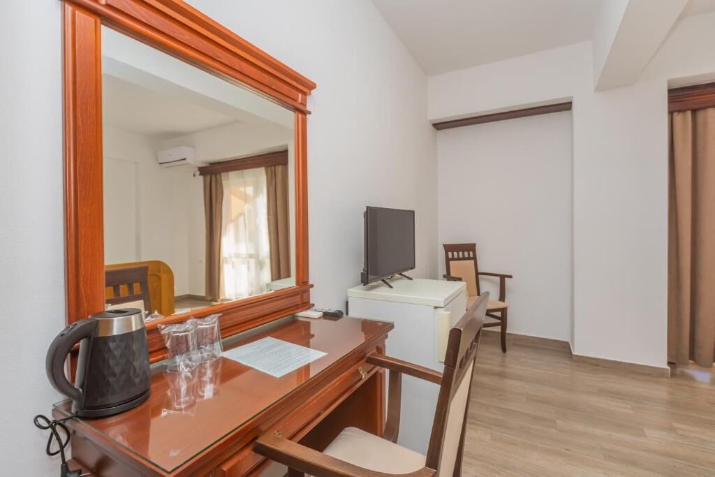 Una habitación de hotel con un escritorio de madera, un televisor, una silla y un espejo grande.
