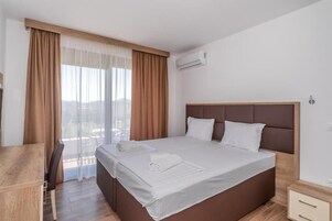 Habitación de hotel con una cama grande, un escritorio y una silla. Se observa un equipo de aire acondicionado en la pared y una ventana con cortinas.
