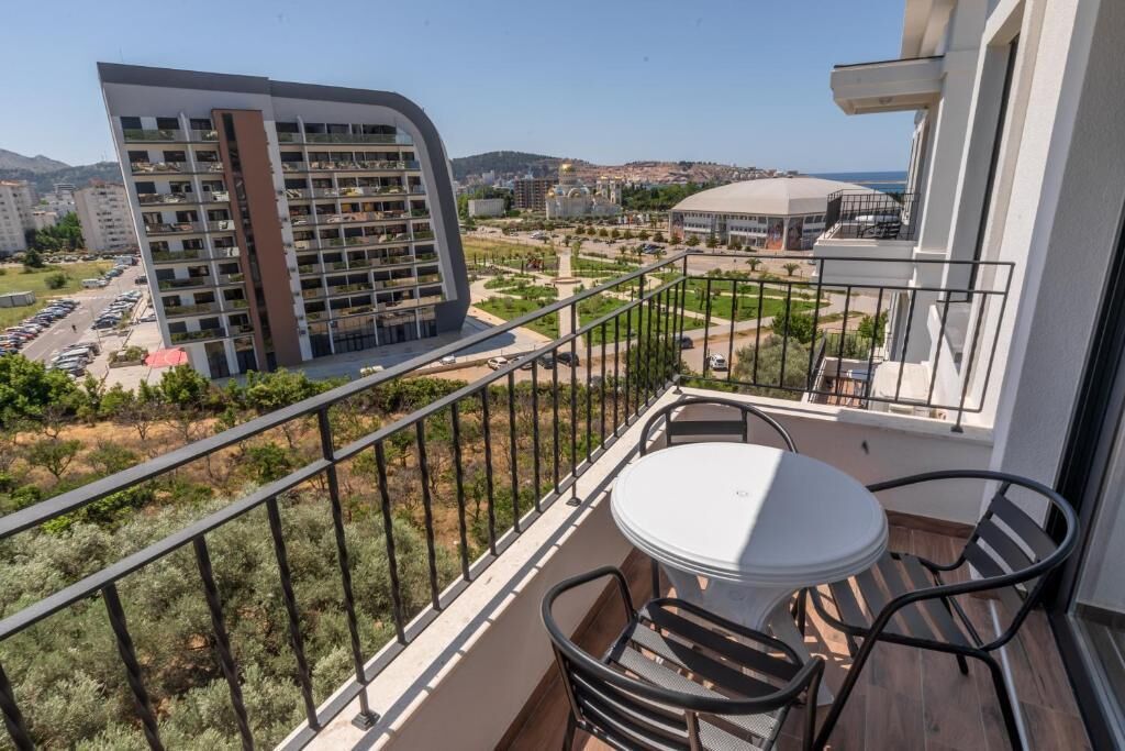 Un balcón con mesa y sillas, con vista a un paisaje urbano con edificios modernos y un estadio.
