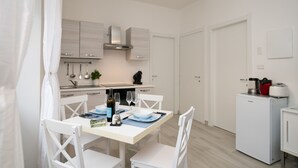 A modern kitchen with white cabinetry, a dining table set for four, and a compact refrigerator. - La Torretta (Moniga del Garda)