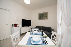 Spiseområde med et bord dækket til to, et fjernsyn og et maleri på væggen.