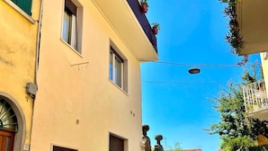 A narrow street with buildings on either side, featuring balconies with potted plants and a clear blue sky. - La Torretta (Moniga del Garda)
