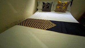 Ein Bett mit weißer Bettdecke, einer schwarz-gelben gepunkteten Decke und zwei Kissen mit geometrischen Mustern.