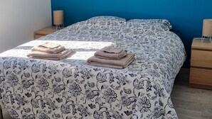 A bedroom with a bed, a nightstand, a lamp, and a wooden floor. - Charming little gîte in the heart of the Baie de Somme (Saigneville)