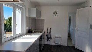 A modern kitchen with a large window, white cabinetry, and a built-in stove. - Charming little gîte in the heart of the Baie de Somme (Saigneville)