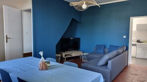 A living room with a TV, sofa, and dining table. - Charming little gîte in the heart of the Baie de Somme (Saigneville)