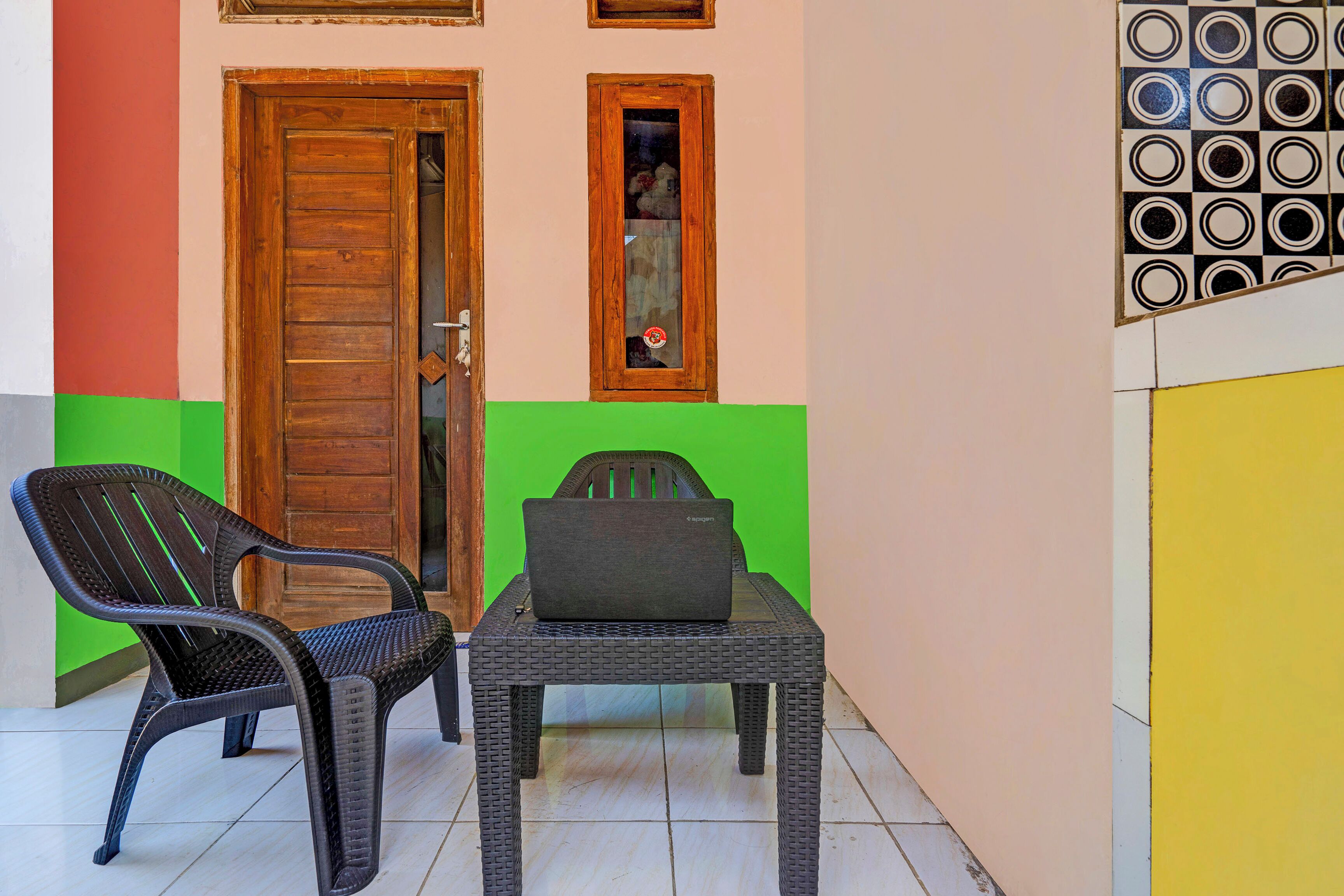A room with a wooden door, a window with a view, a plastic chair, and a table with a laptop.