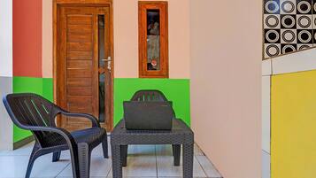 A room with a wooden door, a window with a view, a plastic chair, and a table with a laptop.