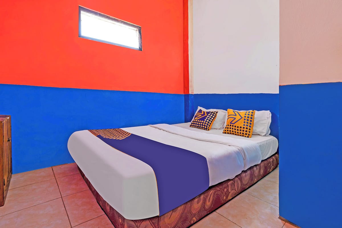 Un lit recouvert d’une couvre-lit blanche et violette, deux oreillers à motifs géométriques et une fenêtre au-dessus du lit.