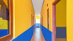 A long, narrow hallway with alternating yellow and blue walls, leading to a bright room at the end. - Hotel O Wisma Dua Putra Syariah (Kertajati)