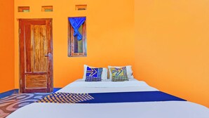 A room with a wooden door, a window with a blue curtain, a bed with patterned pillows, and a blue and white bedspread. - Hotel O Wisma Dua Putra Syariah (Kertajati)