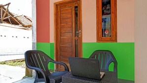 A room with a wooden door, a window with a sticker, and two wicker chairs with a laptop on a table. - Hotel O Wisma Dua Putra Syariah (Kertajati)