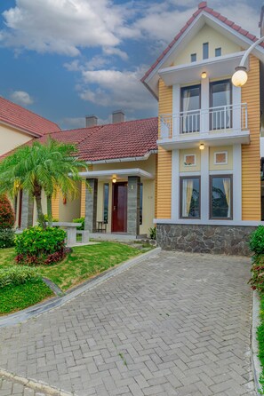 A two-story house with a stone foundation, a red-tiled roof, and a paved driveway.