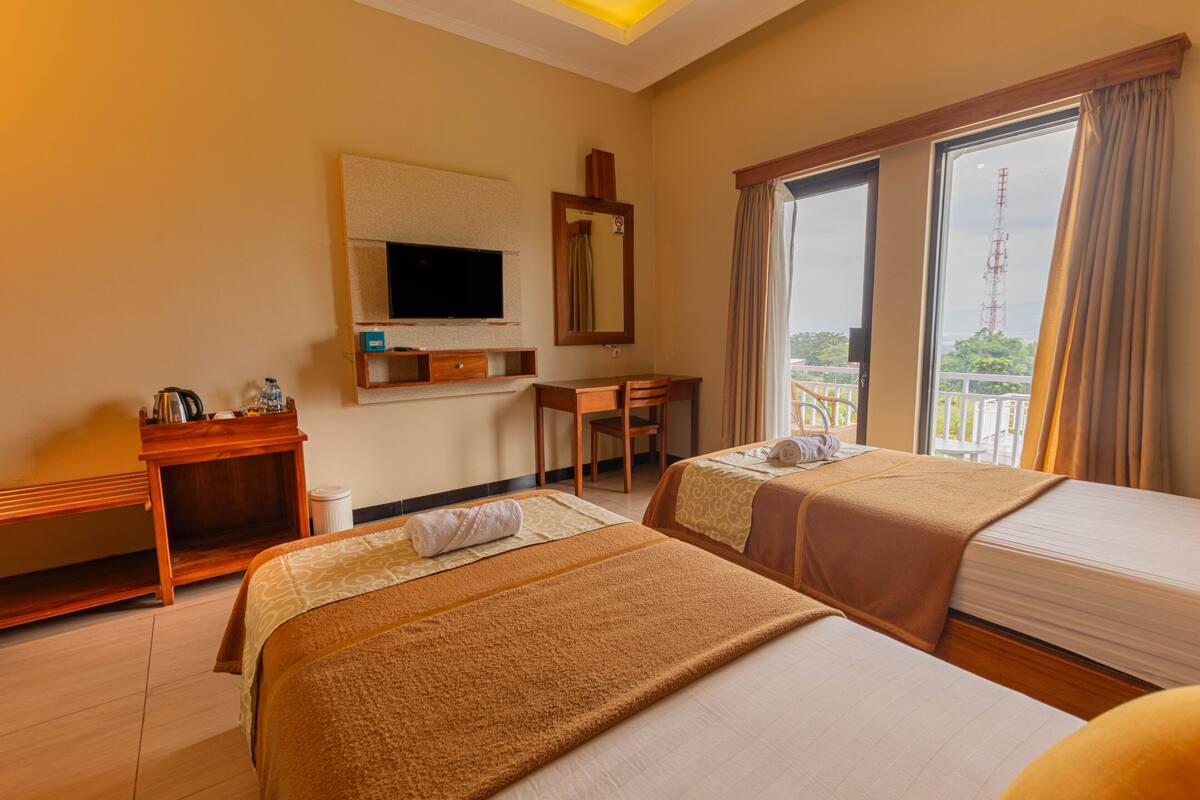 Ein Hotelzimmer mit zwei Betten, einem Schreibtisch, einem Fernseher und einem Balkon mit Blick.