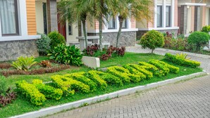Un jardin aménagé avec des haies taillées avec soin, formant le mot « LAXIUS » au premier plan, un chemin de pierre et un bâtiment doté d’une façade en pierre et de fenêtres.