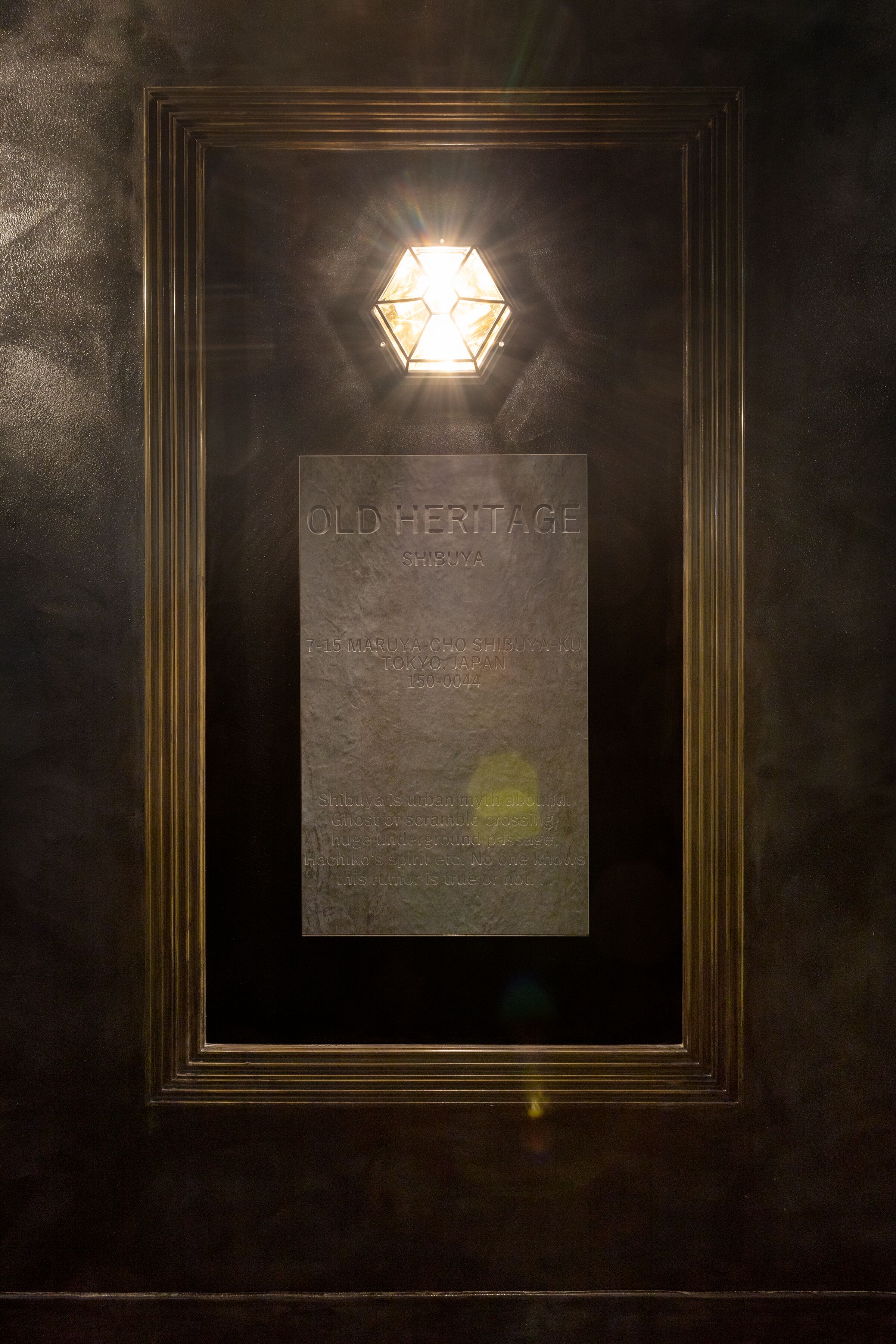 Une plaque encadrée portant l’inscription « OLD HERITAGE SHIBUYA » et un luminaire hexagonal placé au-dessus.