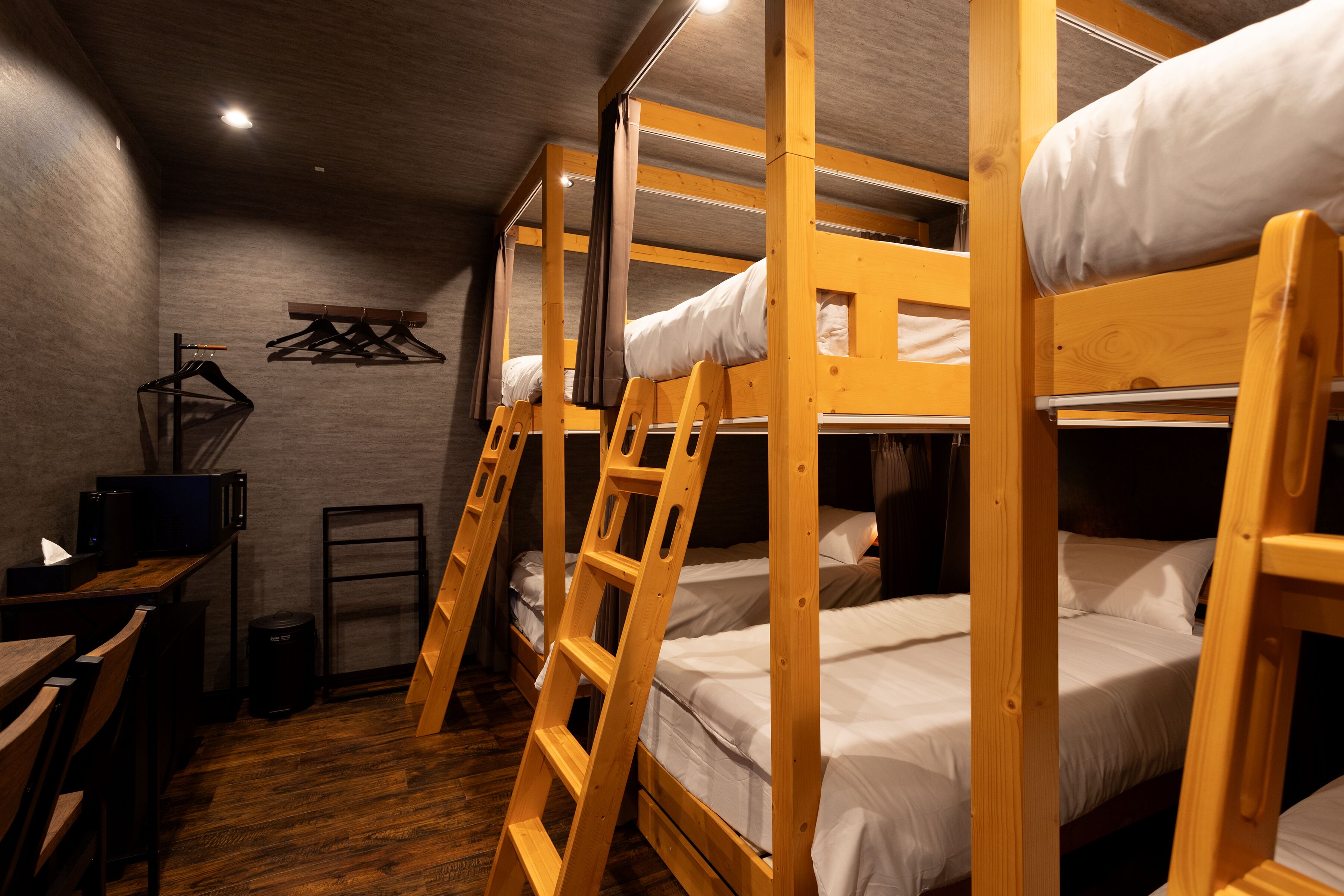 A bunk bed room with wooden frames, a desk, and a chair.