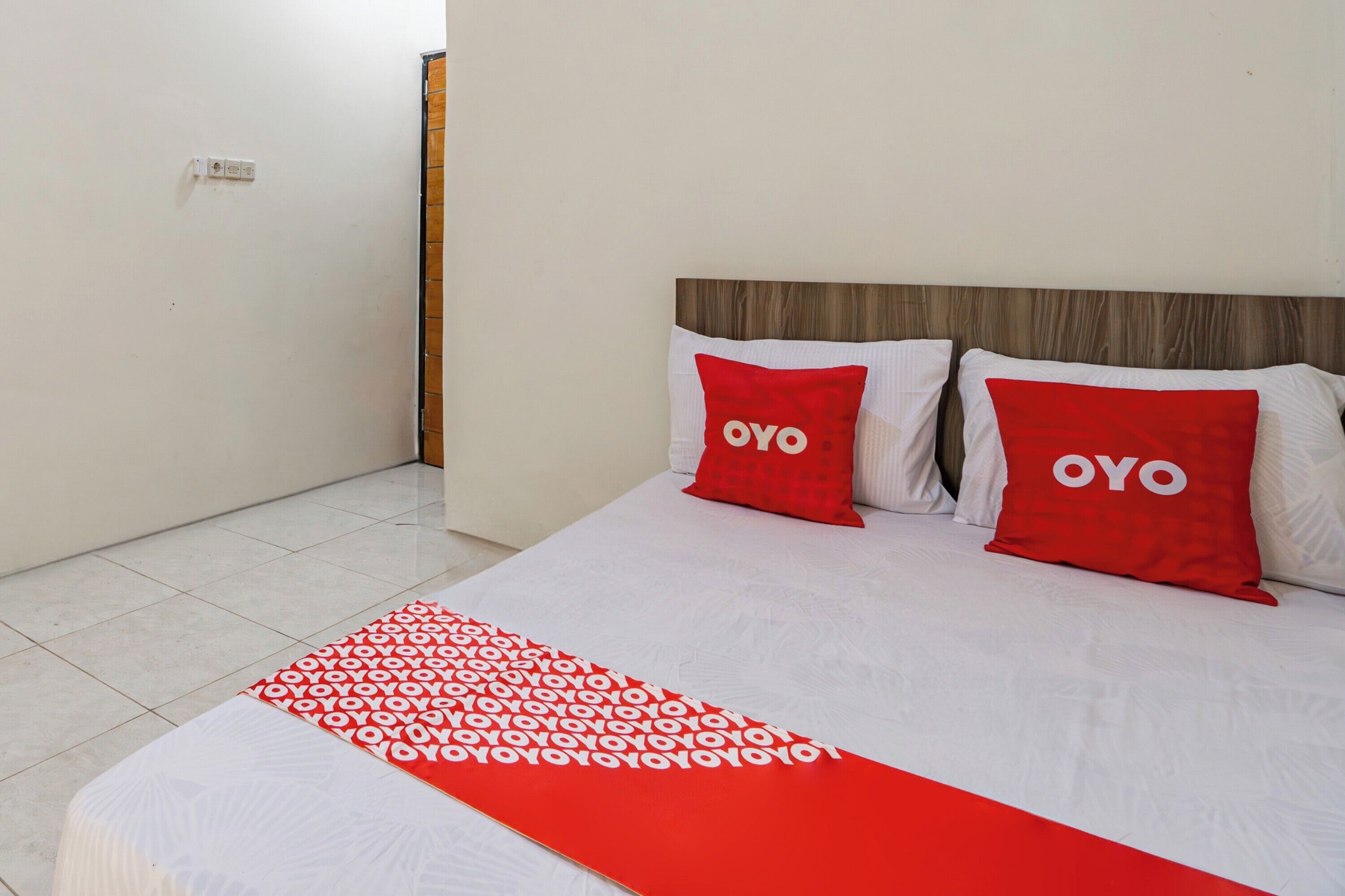 Ett hotellrum med en säng, två röda kuddar med ordet ”OYO” på, och en röd och vit mönstrad sängkappa.