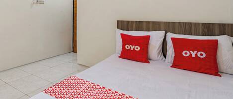 A hotel room with a bed, two red pillows with the word "OYO" on them, and a red and white patterned bed runner.