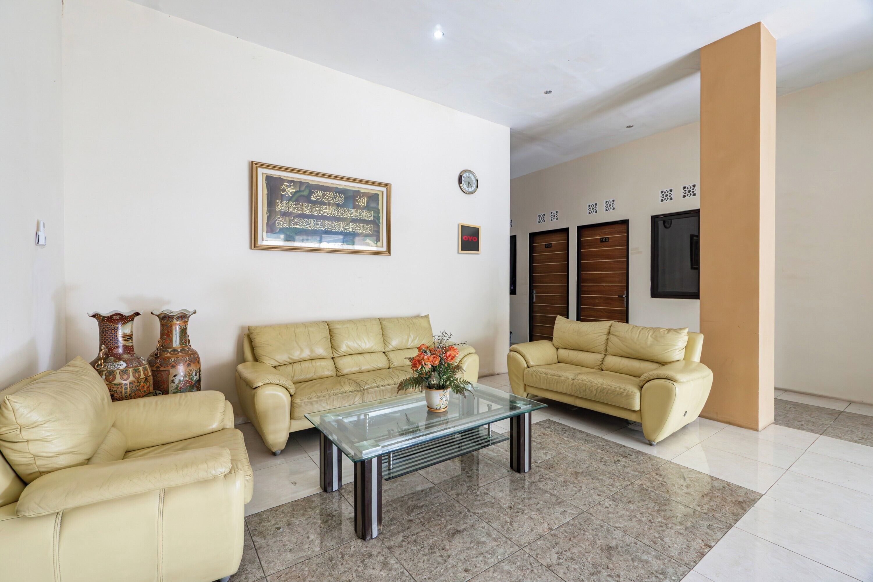A modern living room with two beige leather sofas, a glass coffee table, decorative vases, and a framed artwork on the wall.