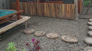 Une structure en bois comprenant un banc et une table, entourée de gravier et de plantes.