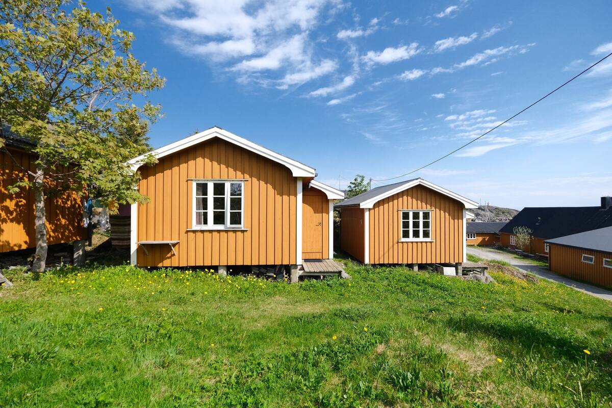 Two wooden cabins with white trim, set in a grassy area with a clear sky.