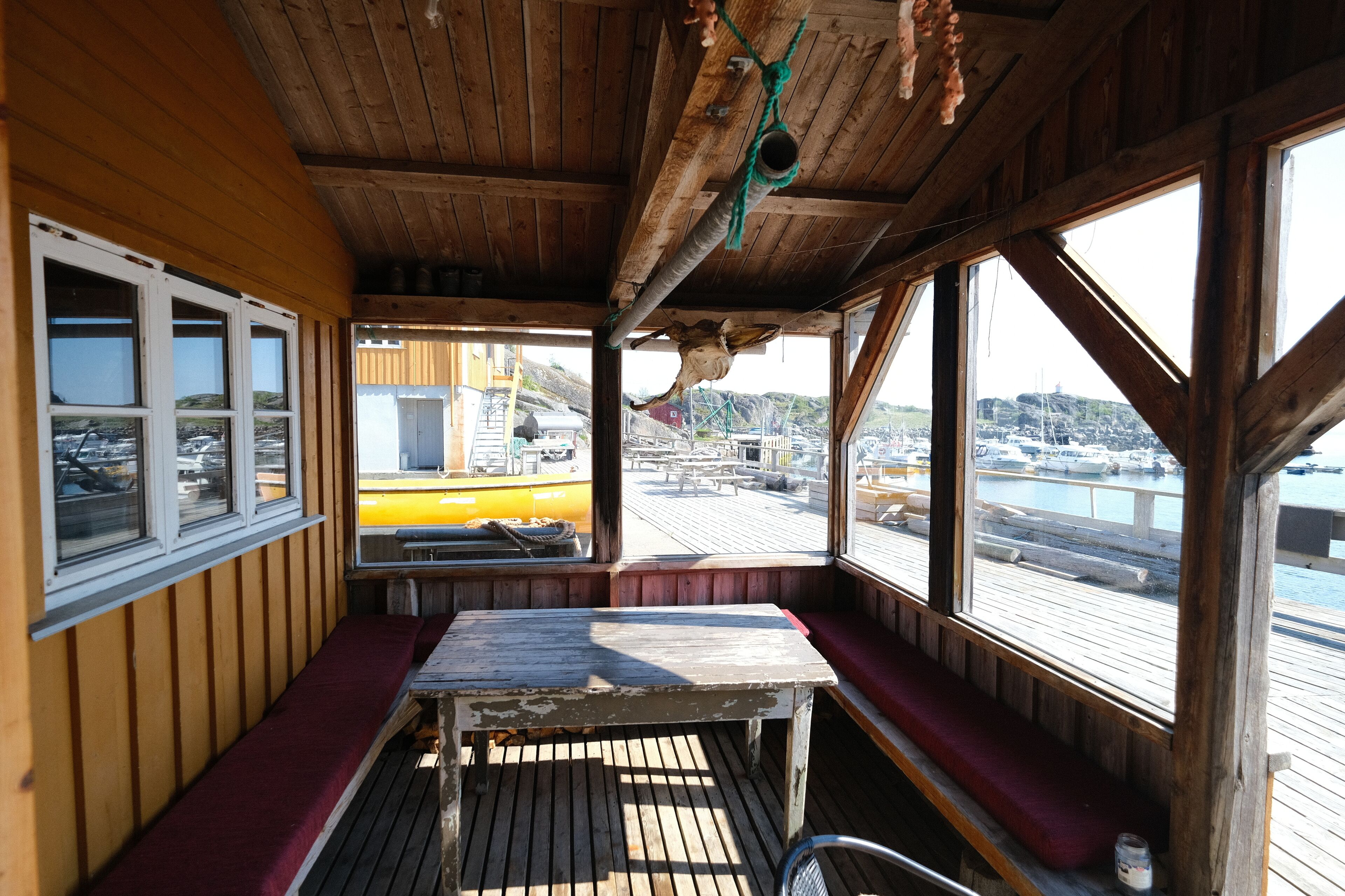A wooden cabin with a bench, a table, and a view of a dock and boats.