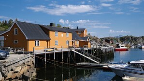 Un bâtiment en bois avec une jetée s’avançant dans une eau calme, entouré de bateaux et sous un ciel dégagé.