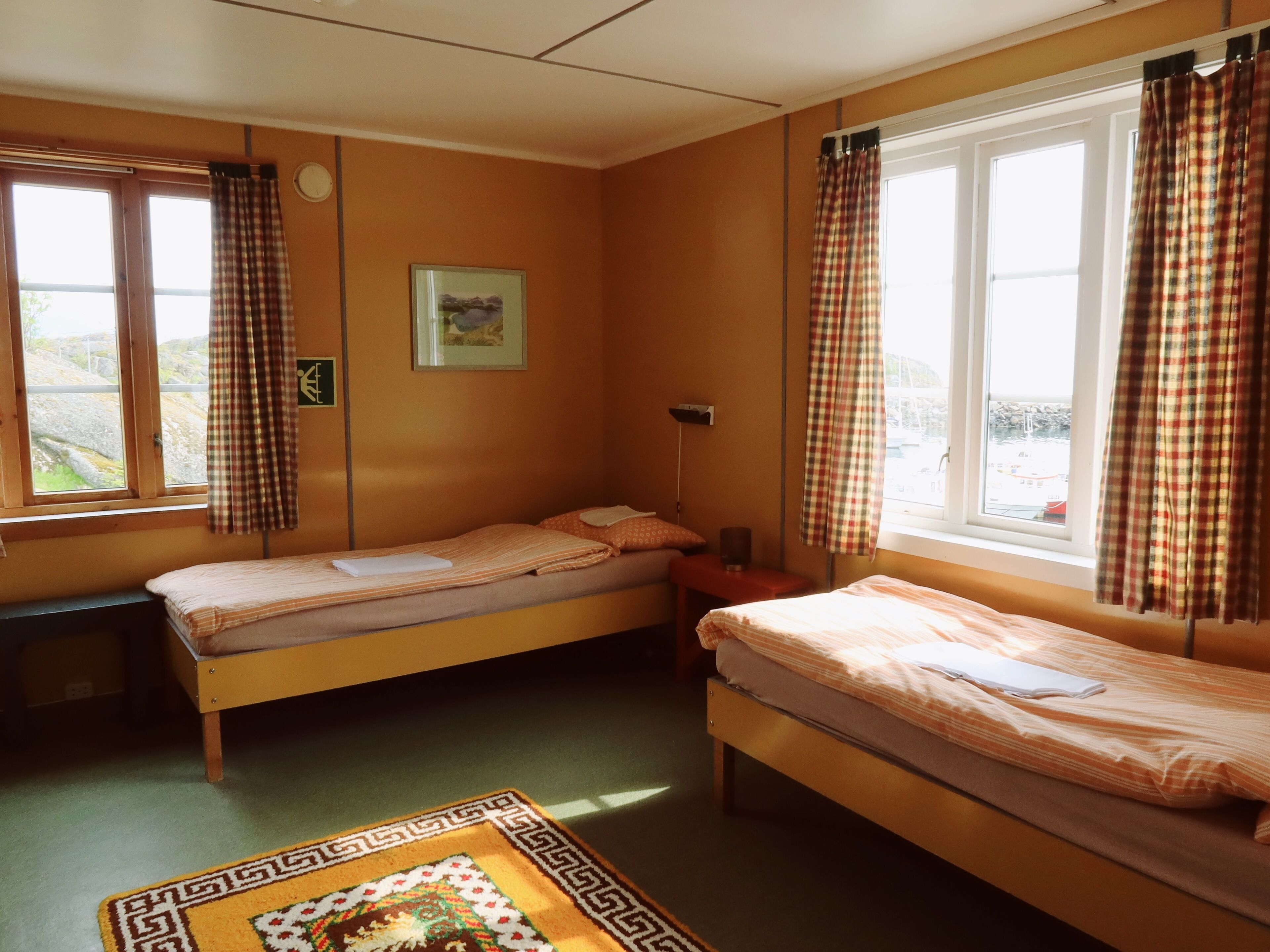 Una habitación con dos camas individuales, un escritorio pequeño, una silla, una lámpara y una ventana con cortinas.