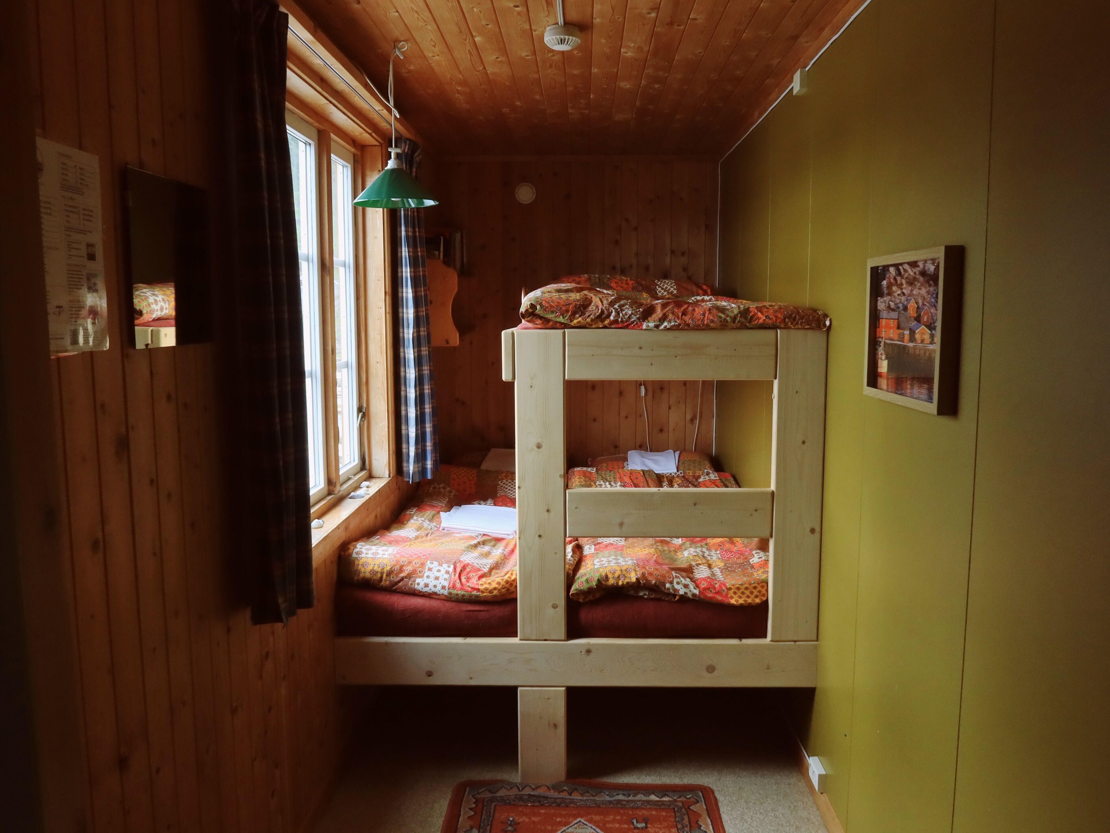 A bunk bed with colorful bedding, a window with curtains, a green wall, and a small rug.
