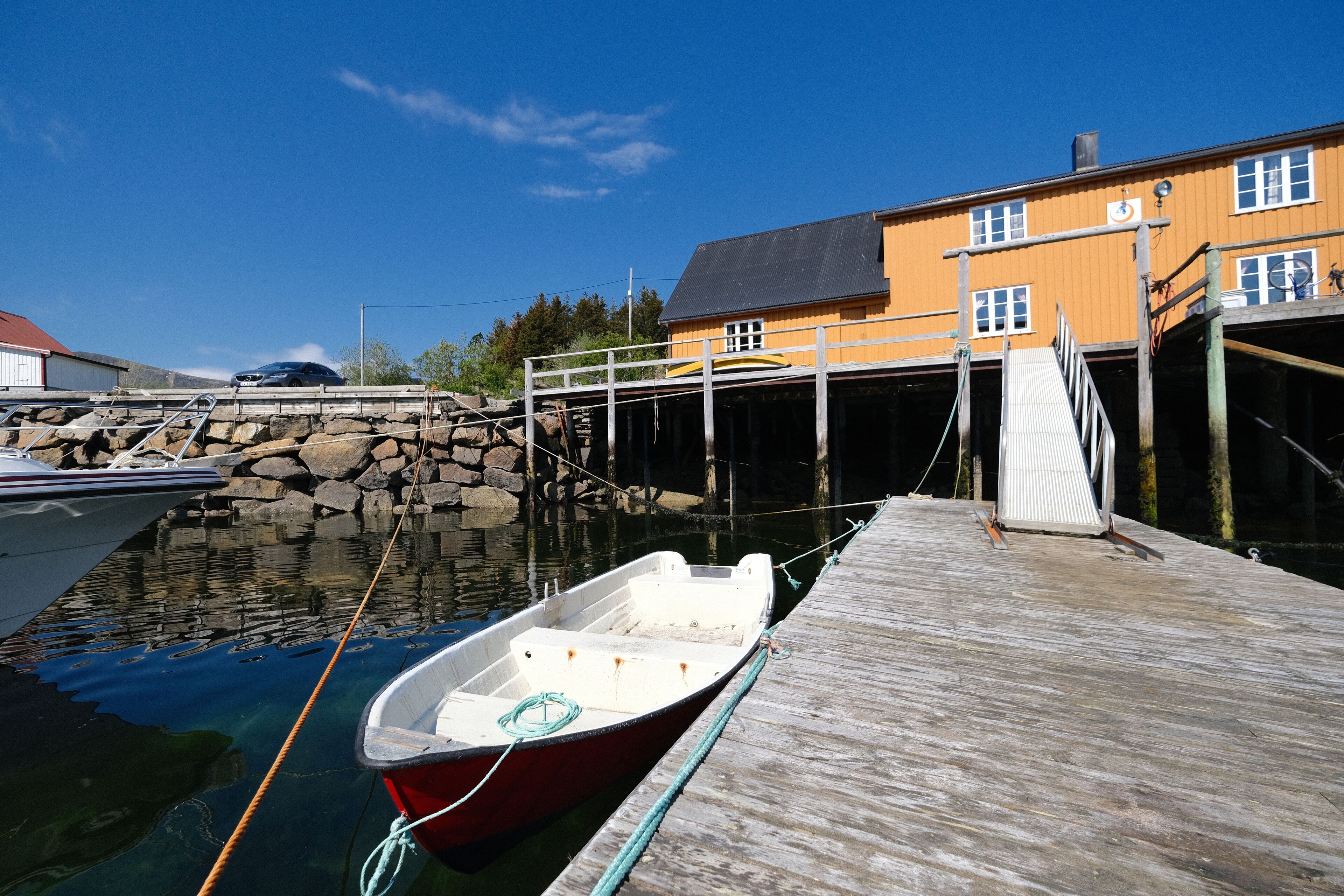 A dock with a small boat tied to it, a wooden pier, and a yellow building in the background.