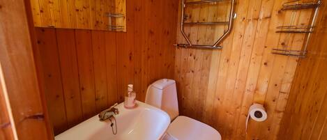 A wooden-paneled bathroom with a white sink, toilet, and metal towel rack.