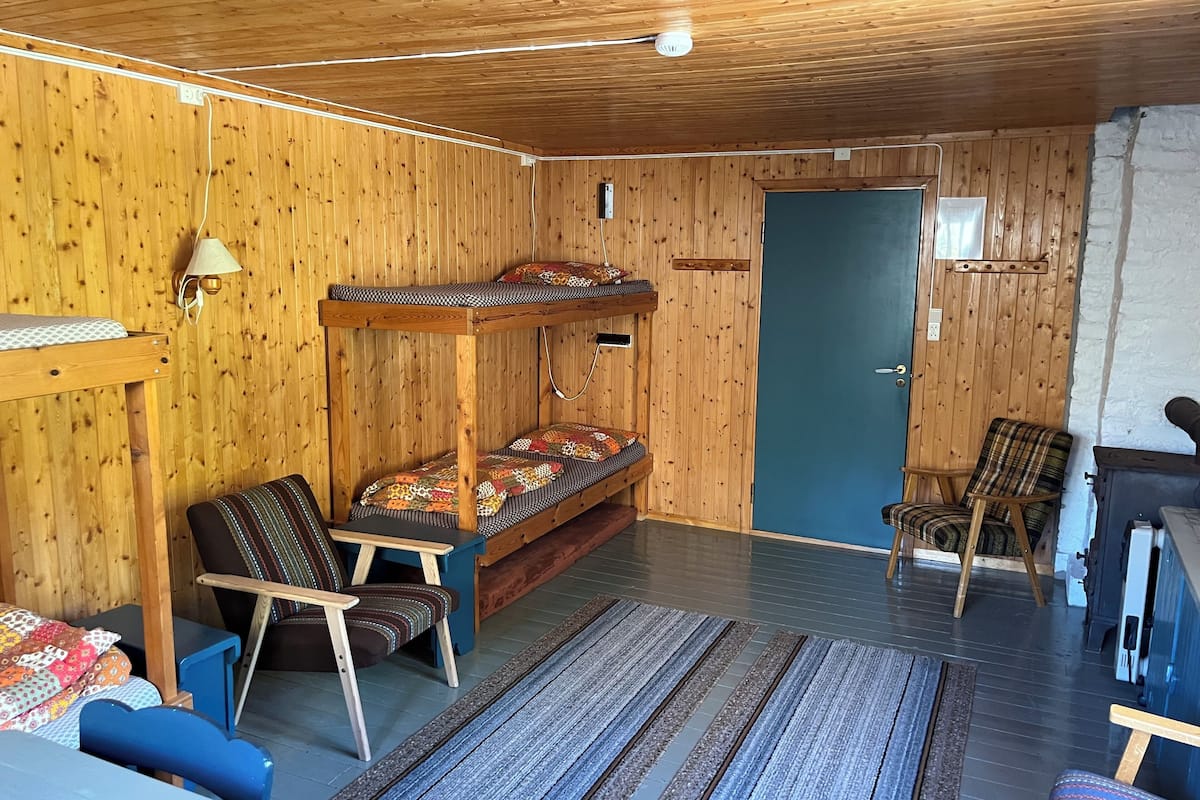 A cozy room with a bunk bed, two chairs, a small table, and a door.