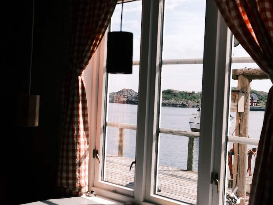 A room with a large window overlooking a body of water, a wooden dock, and a checkered curtain.