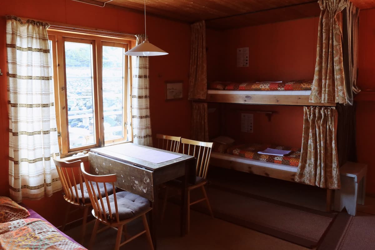 A small, cozy room with a bunk bed, a desk with a chair, and a window with curtains.