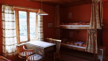 A small, cozy room with a bunk bed, a desk with a chair, and a window with curtains.