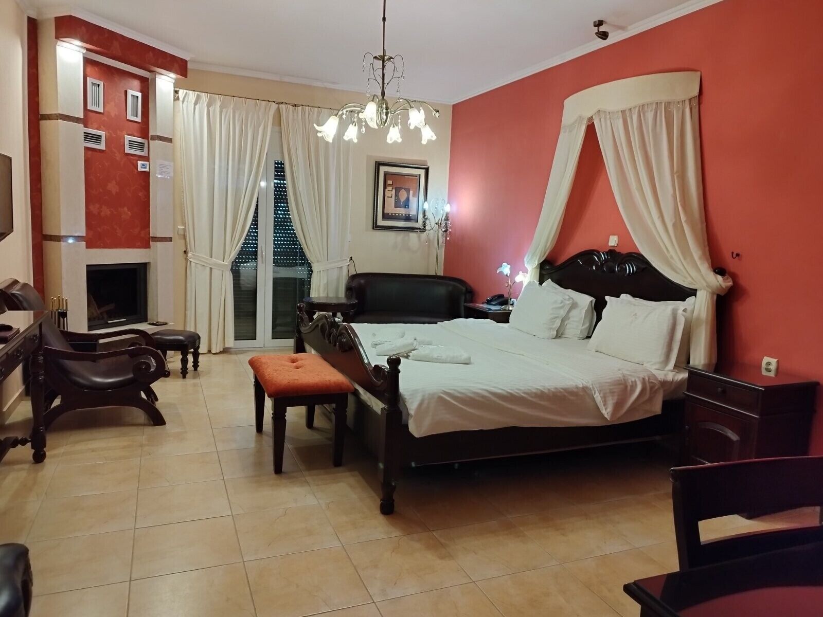 A hotel room with a bed, a desk, a chair, a fireplace, and a view of a building outside.